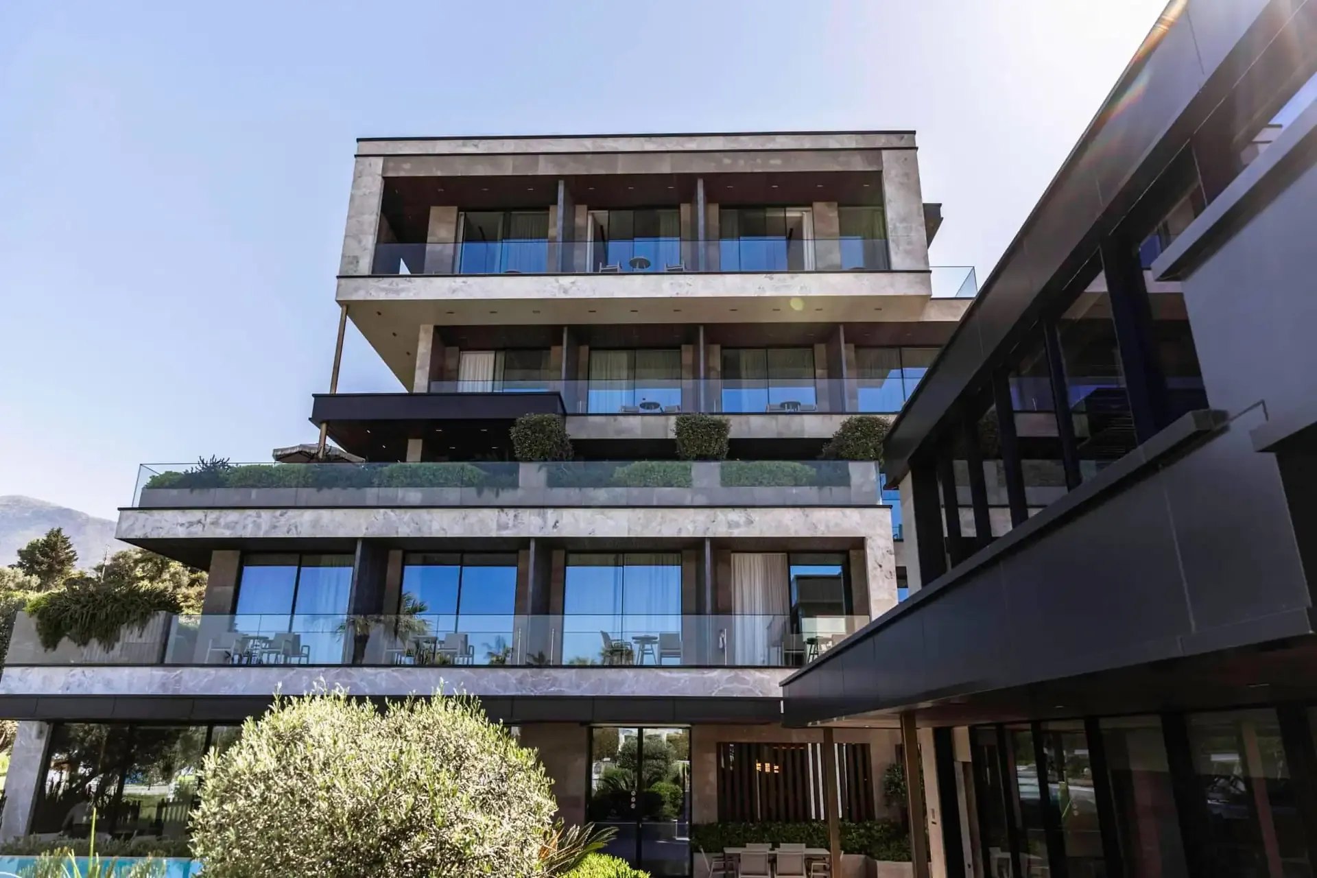 The stone-clad front of Prado Luxury Hotel, each floor set back from the one below, planting standing on the ledges and glass balustrades along every balcony