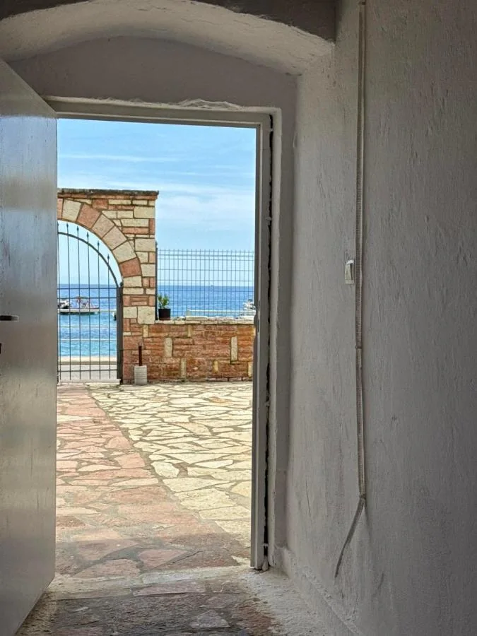 Looking out of a whitewashed passage through an open door to the stone arch, the sea wall and the turquoise bay beyond