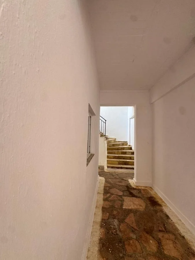 Whitewashed passage with a small window and pale stone steps rising to the upper floor