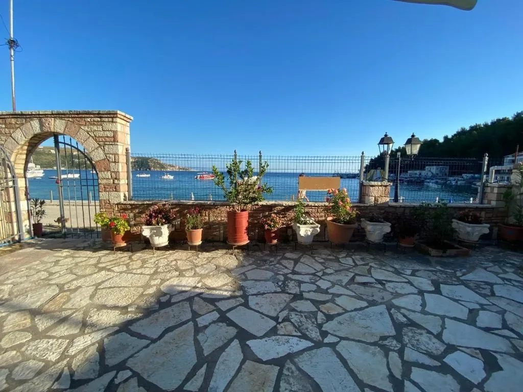 Flagstone terrace with planters along a low stone wall, the arched gateway on the left and the bay and moored boats beyond