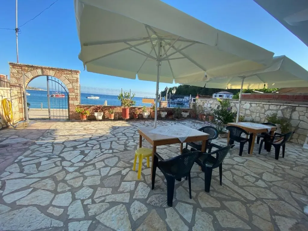 Terrace tables and chairs under a cream parasol, the arched gateway and the sea behind them