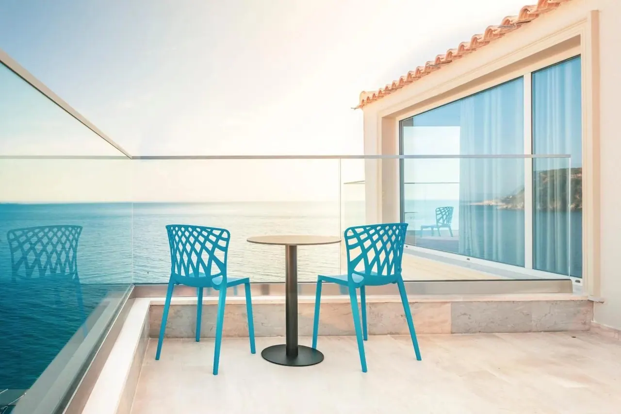 A balcony with turquoise chairs, a glass balustrade, terracotta pantiles and the sea