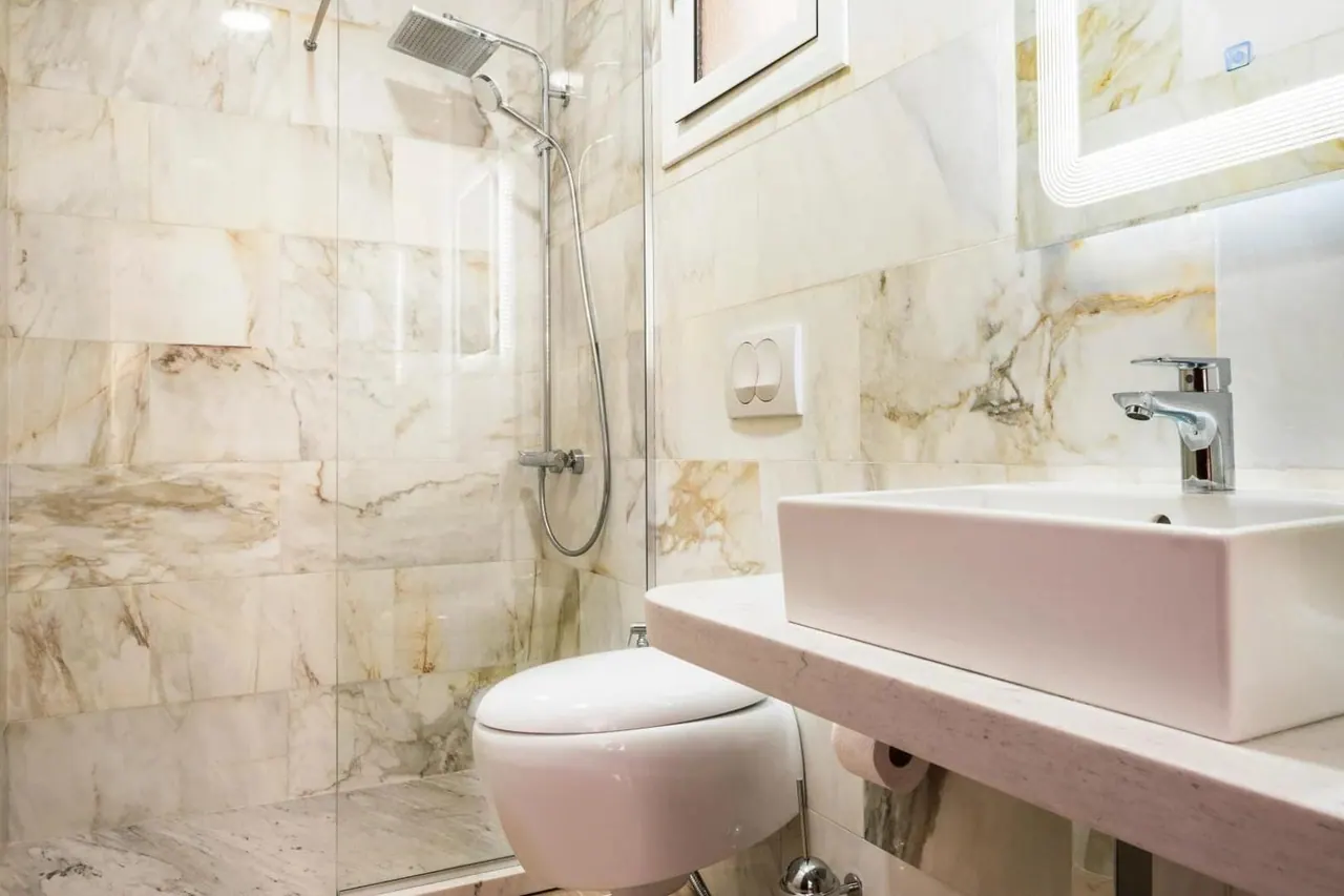 A bathroom clad in honey-veined marble with a walk-in shower and a rectangular vessel basin