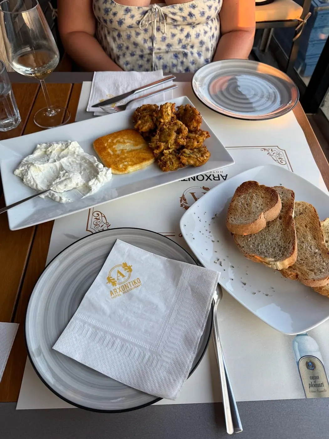 A folded napkin printed with the gold ARXONTIKO monogram on a stacked grey plate