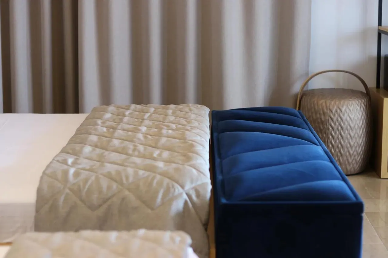 A quilted bed cover and a deep blue upholstered bench at the foot of the bed
