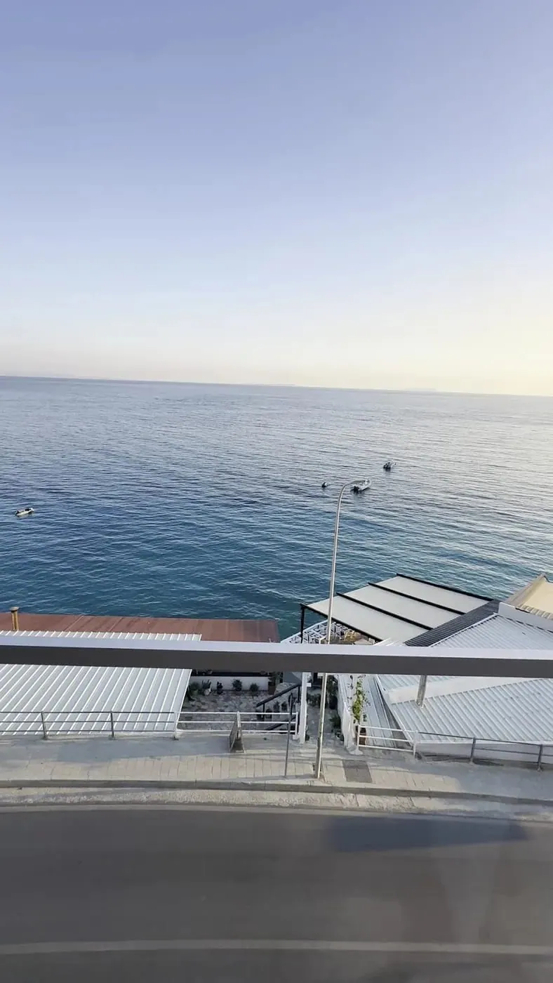 Flat open sea from an upper floor, three boats moored offshore and the beach roofs below