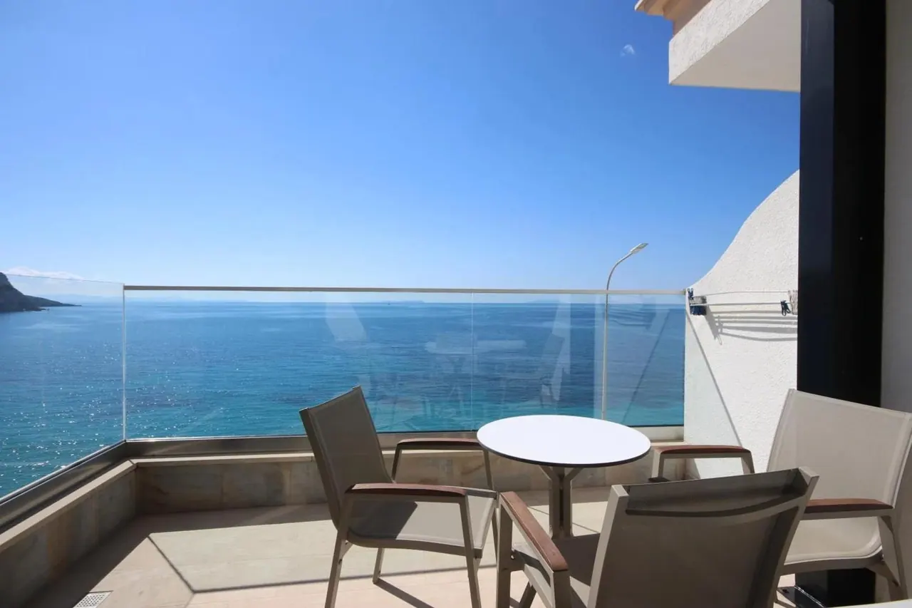 A terrace with two mesh chairs and a round table behind a glass balustrade, looking out over the sea