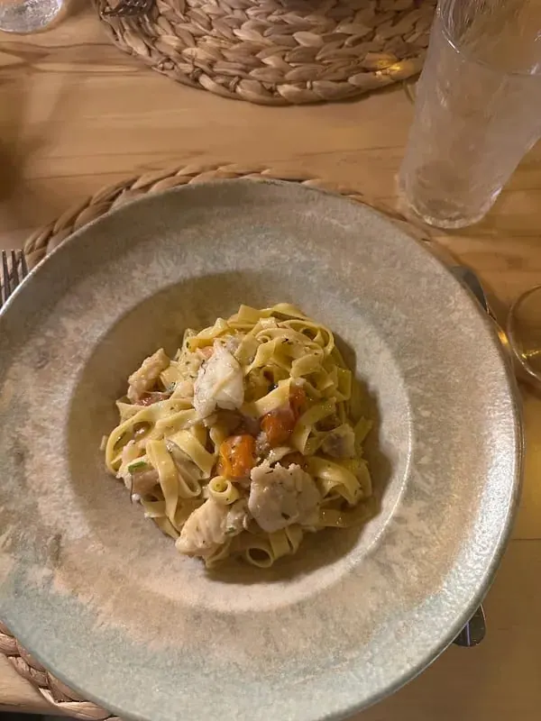 Tagliatelle with pieces of white fish and cherry tomatoes in a wide speckled stoneware bowl on a woven mat