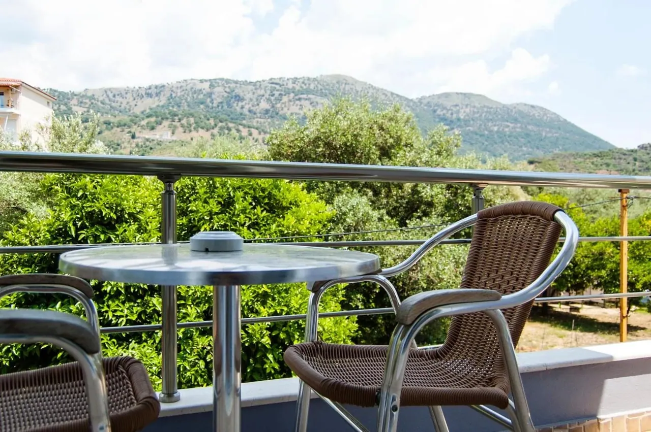 Wicker chairs and a metal table on a balcony above dense olive and citrus