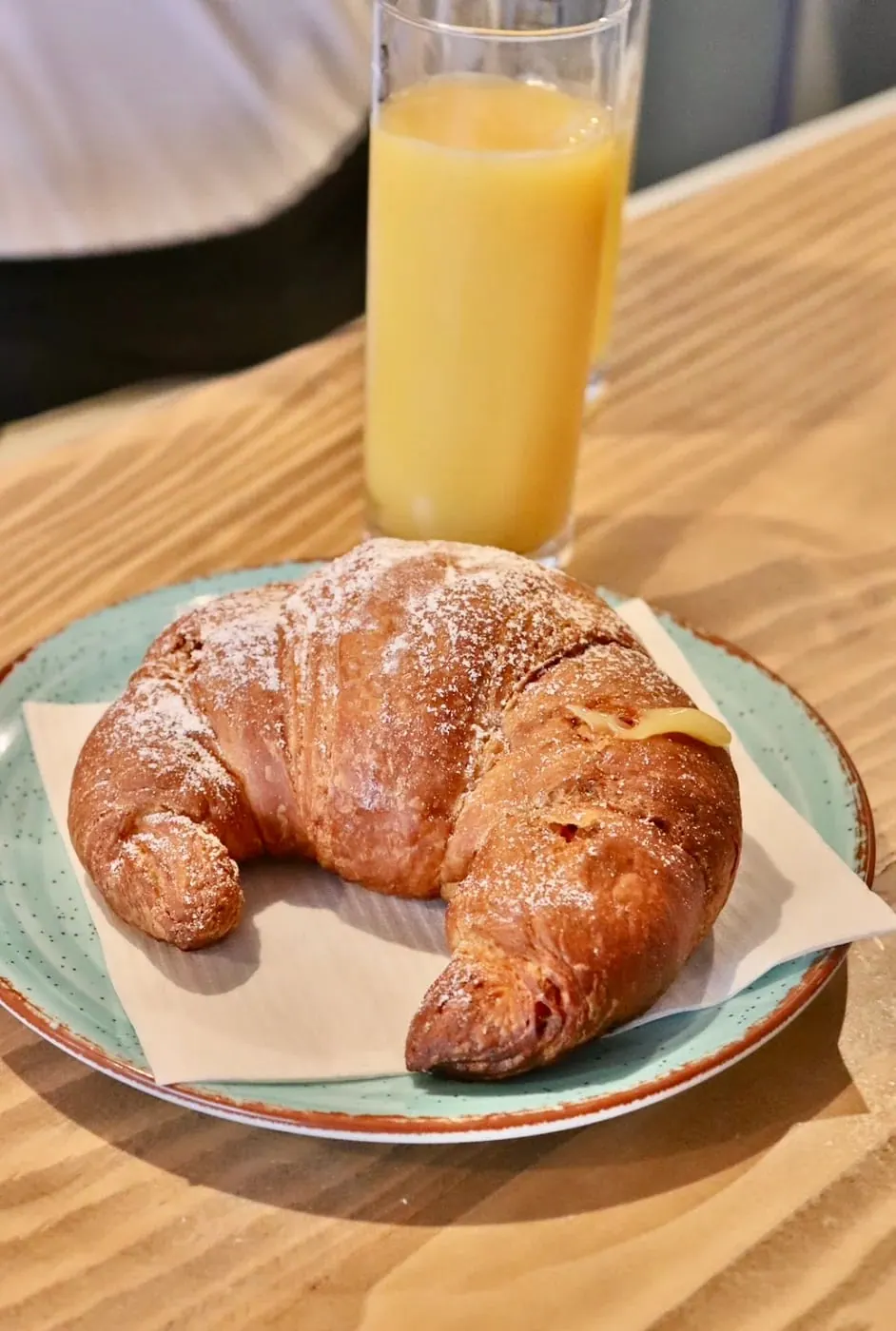 A croissant dusted with sugar on a green plate beside orange juice