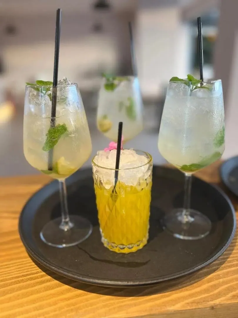 Three stemmed drinks with mint and crushed ice, and a short yellow cocktail, on a dark tray