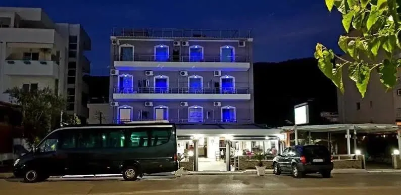The hotel facade at night, every balcony washed in blue light above the lit restaurant terrace