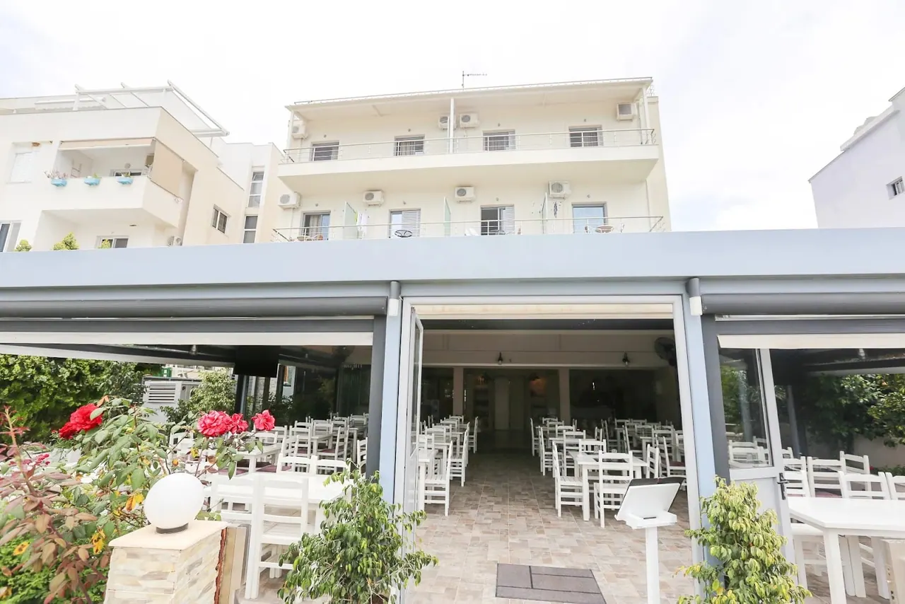 White chairs and tables set out under the hotel's canopy in daylight, with the building rising behind
