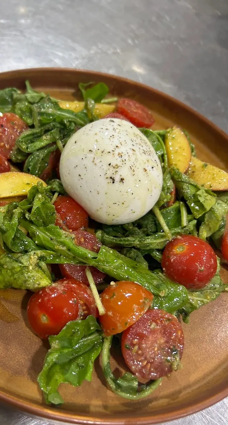 A whole burrata on dressed rocket with cherry tomatoes and peach slices