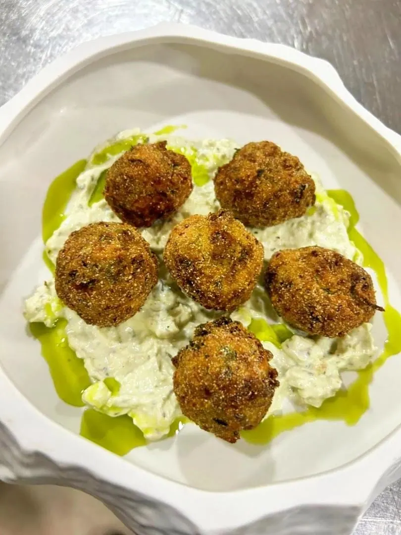 Six fried croquettes on a chunky herbed white dip, dressed with green oil