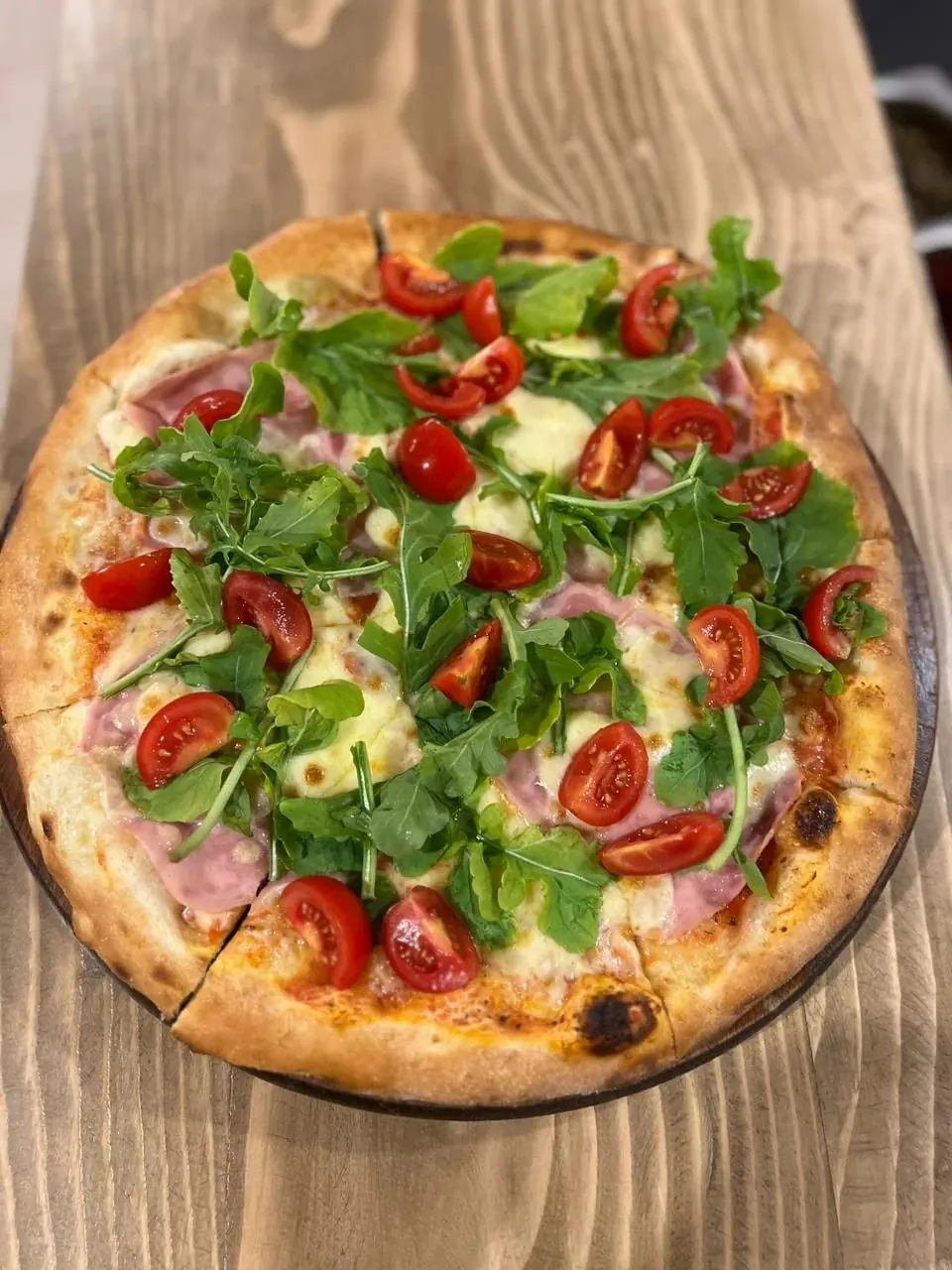 A pizza with cooked ham, mozzarella, rocket and halved cherry tomatoes on a wooden board