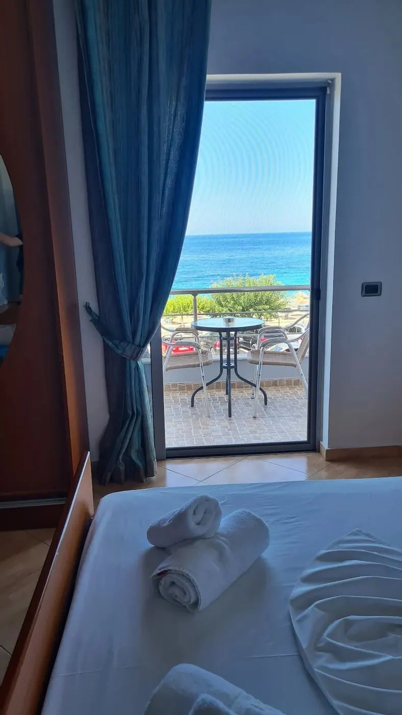 A bed beside an open balcony door, with the coast road, the beach and the sea through it