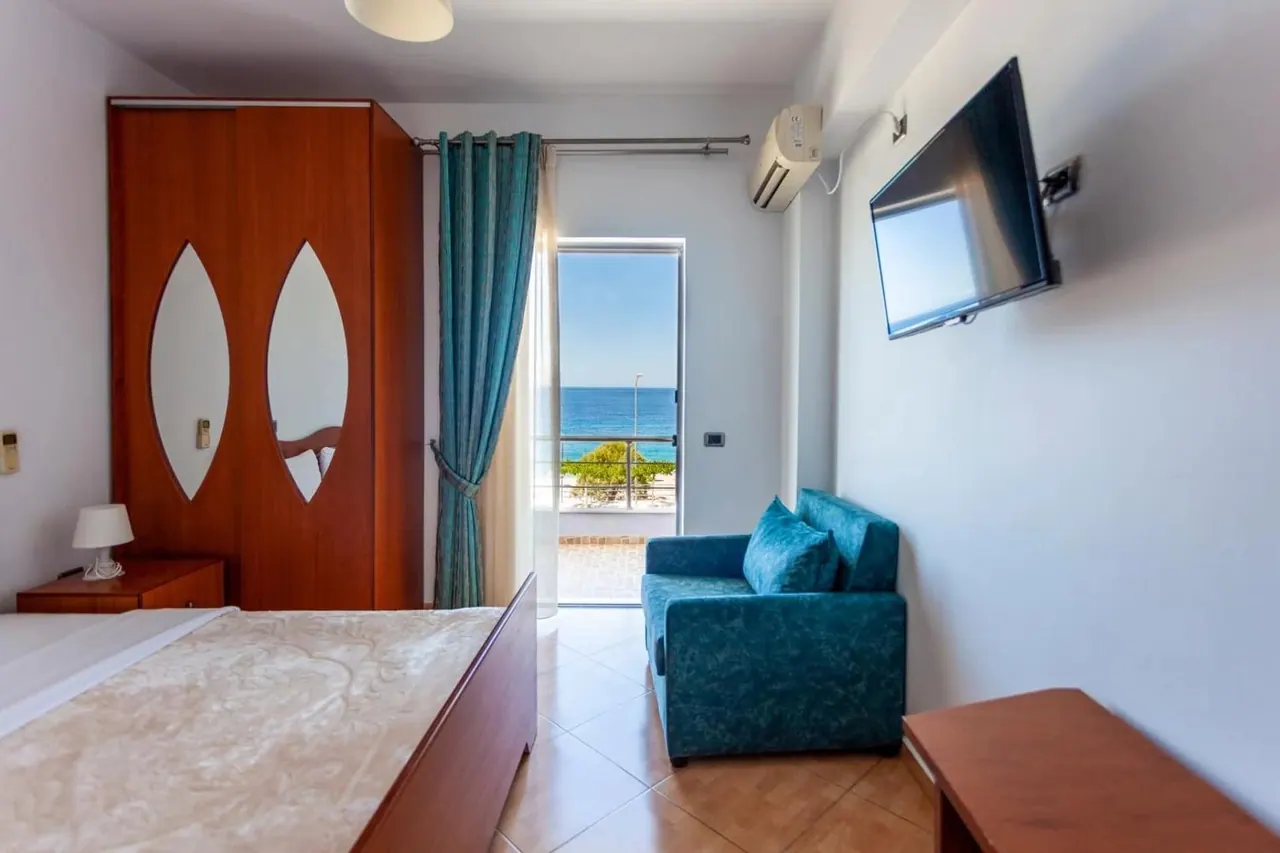 A hotel room with a teal sofa and a balcony door standing open onto the sea