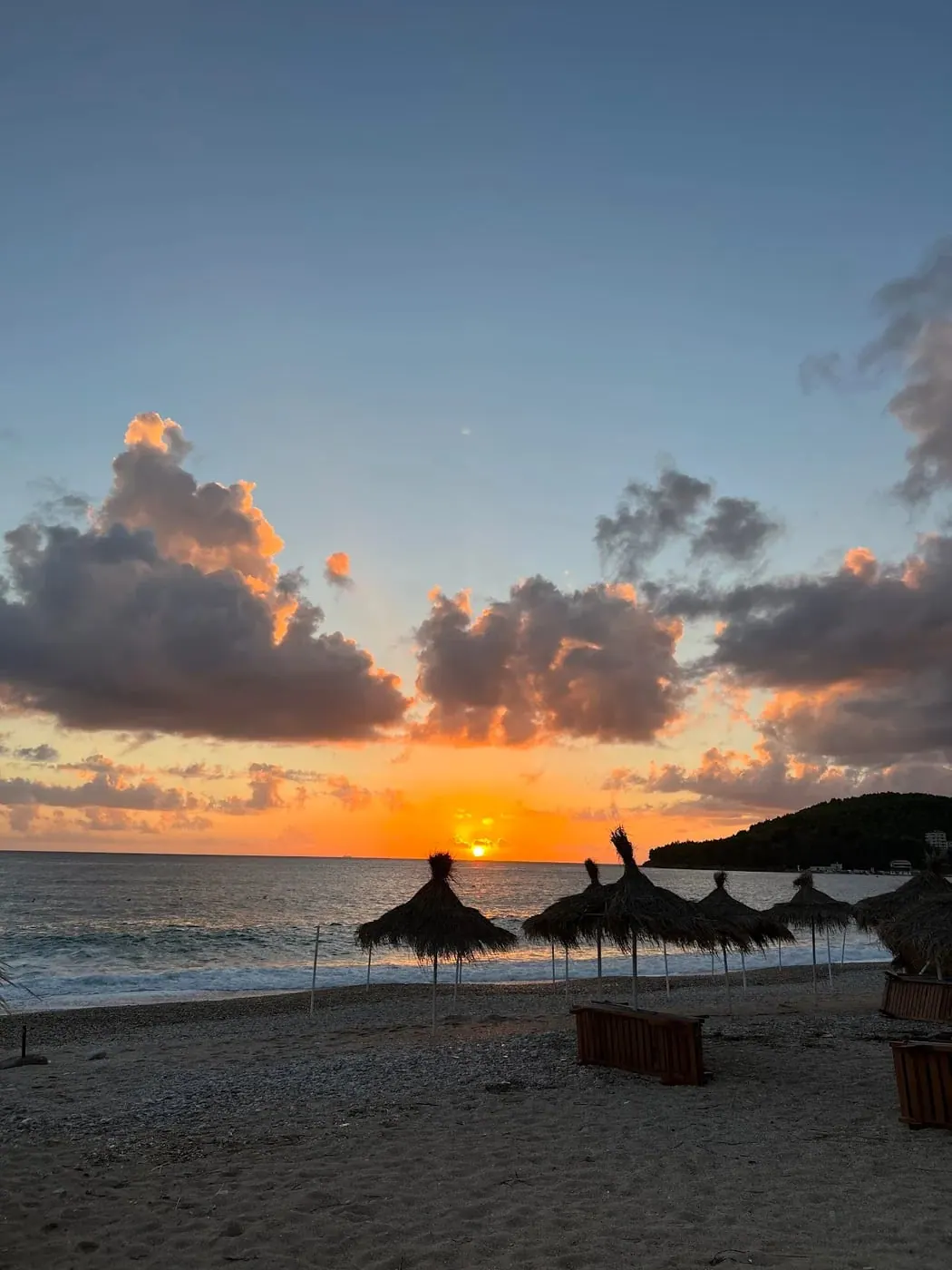 A wide sunset over the bay with cloud banks above the water and umbrellas on the shore