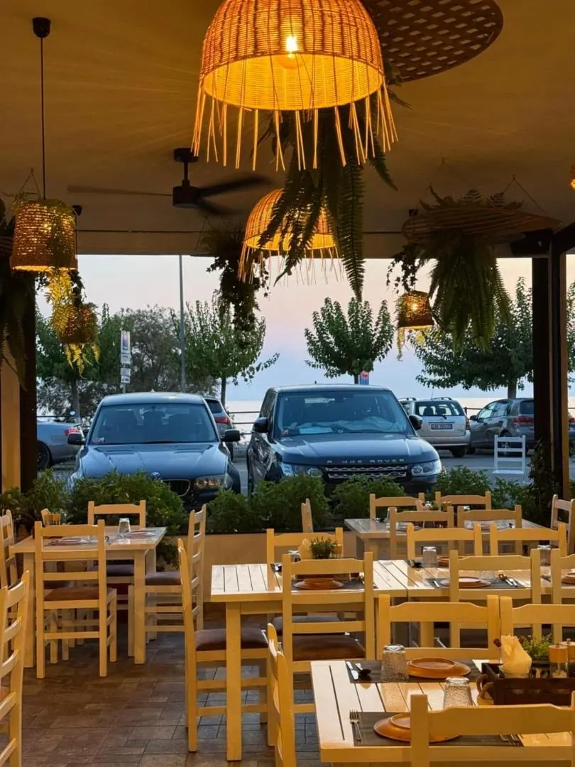 Woven lantern shades over set tables on the terrace at dusk, cars parked beyond