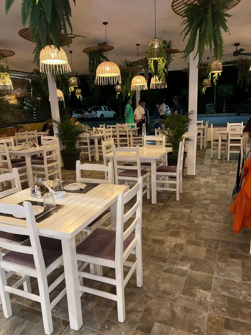 Long rows of white tables and chairs under woven pendant lamps on the restaurant terrace