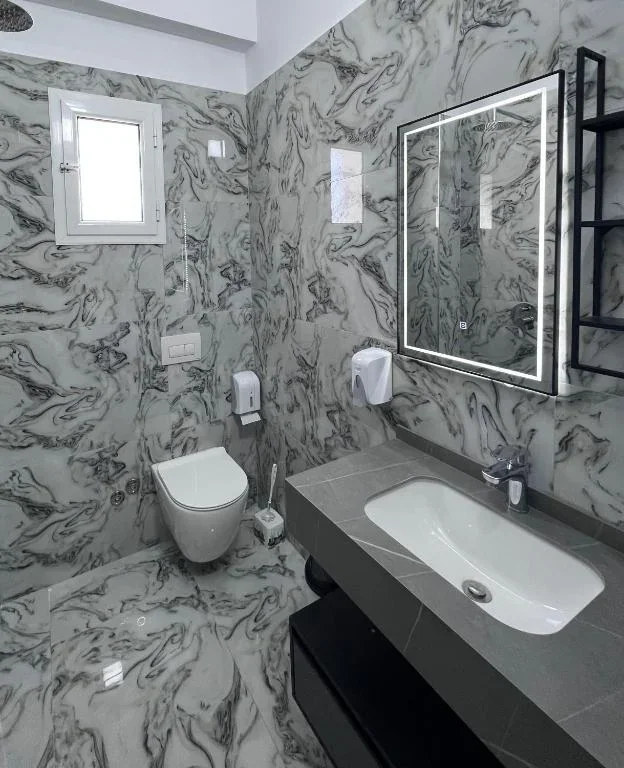 A bathroom at Hotel Frida clad in heavily veined marble, with a lit mirror
