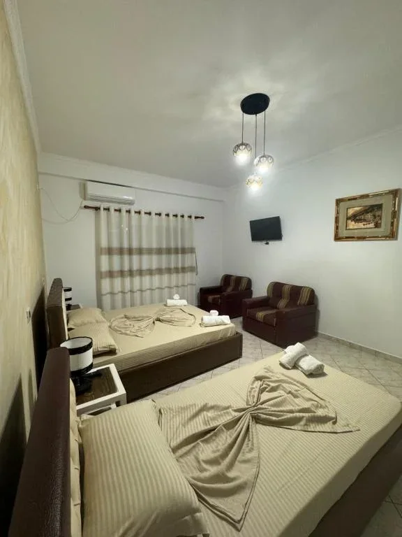 A room at Hotel Frida with two beds either side of a bedside table, two armchairs and a wall-mounted television showing football
