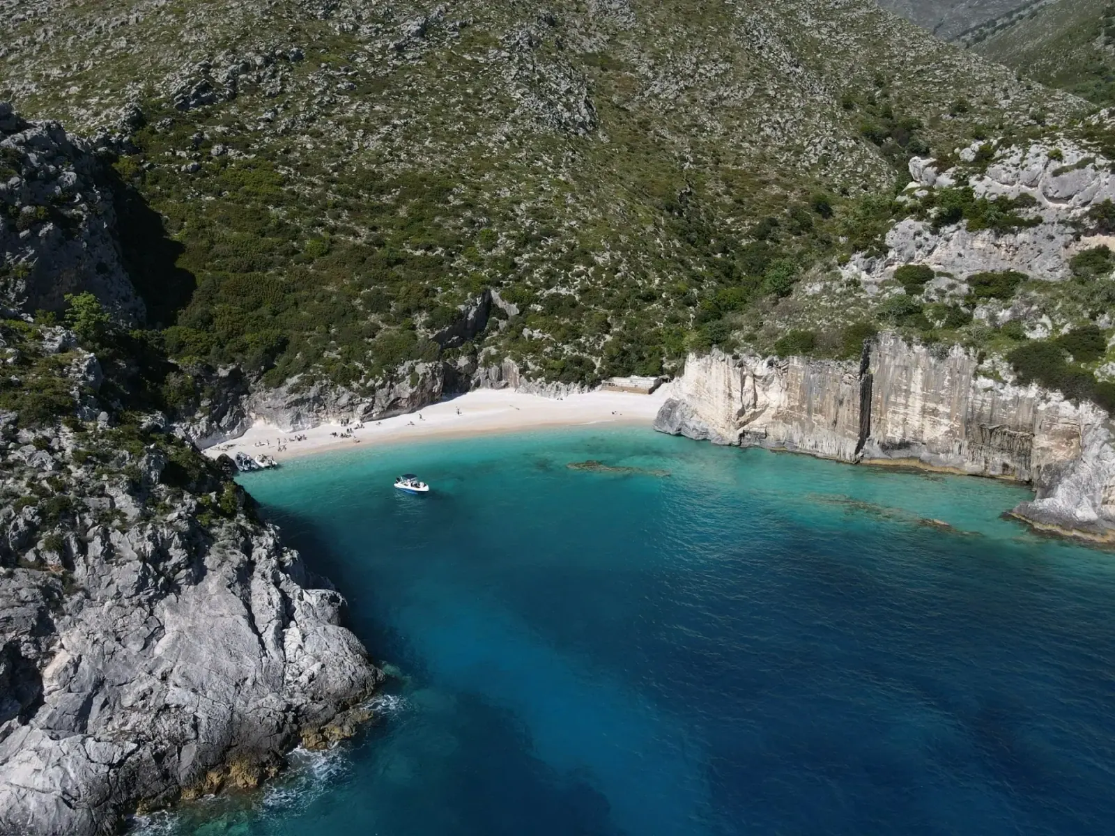 Aerial view of a turquoise cove with a boat and white-pebble beach on the Albanian Riviera near Himara