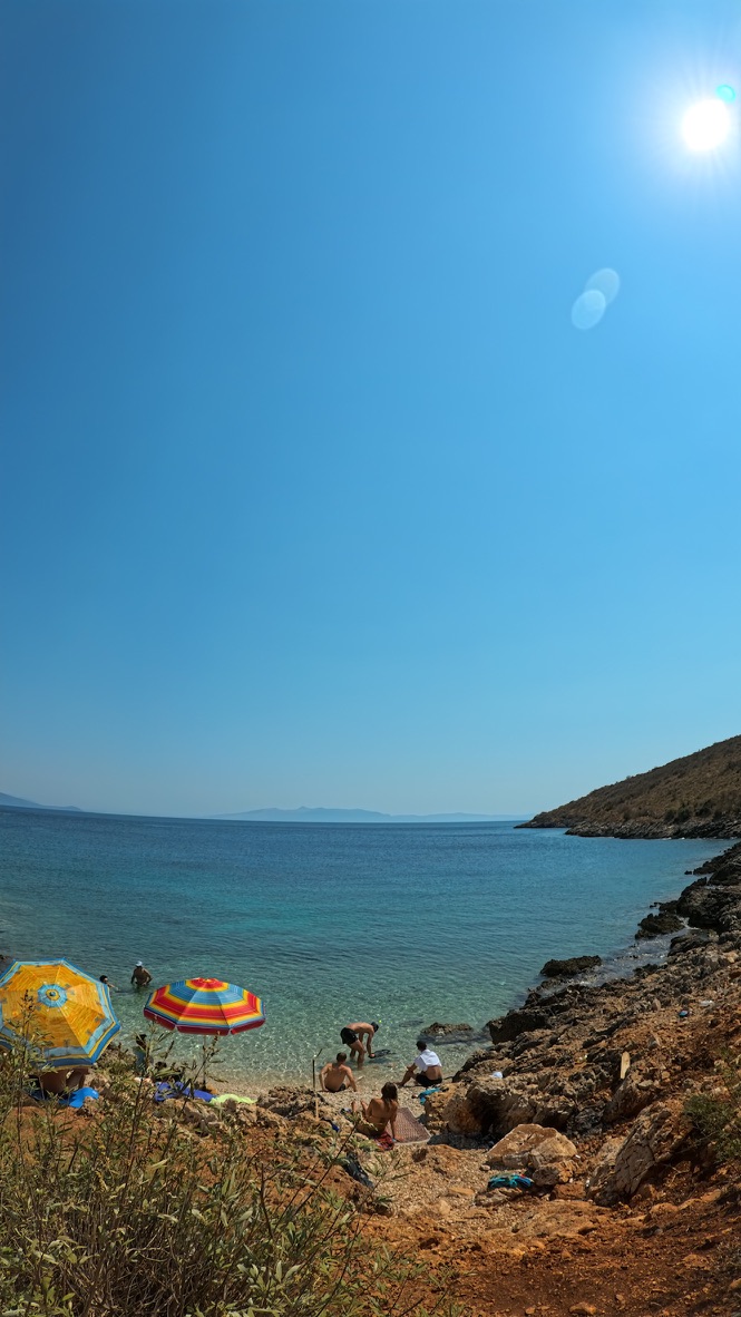 Busy beach club bay on the Himara Riviera with umbrellas and turquoise water where watersports are rented