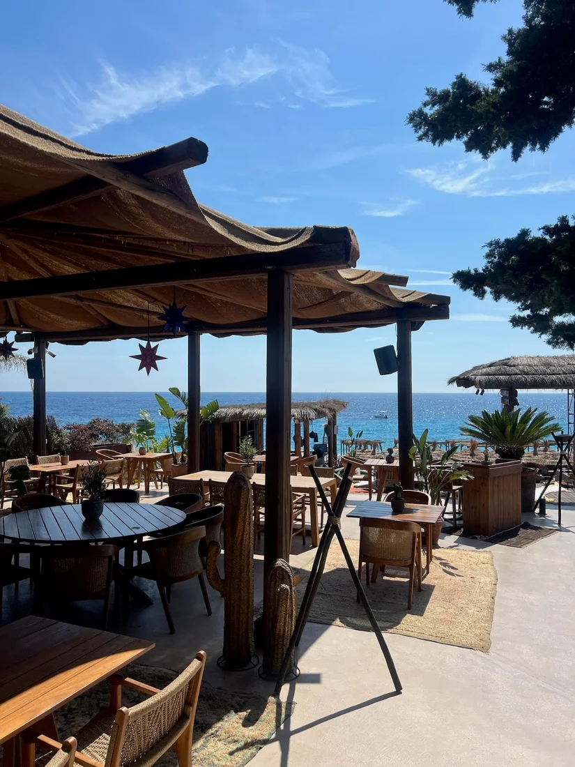Moyo Drymades beach club terrace with thatched umbrellas and wooden tables overlooking the Ionian Sea at Drymades