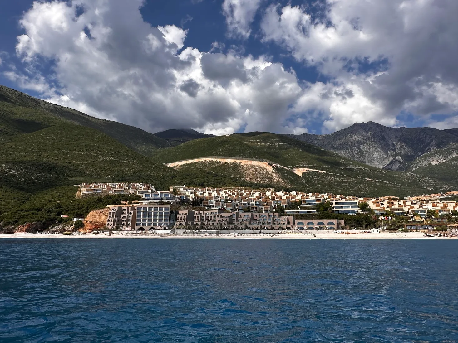 Green Coast development seen from the sea in Palasë, Albania, with the resort buildings and beach below the mountains