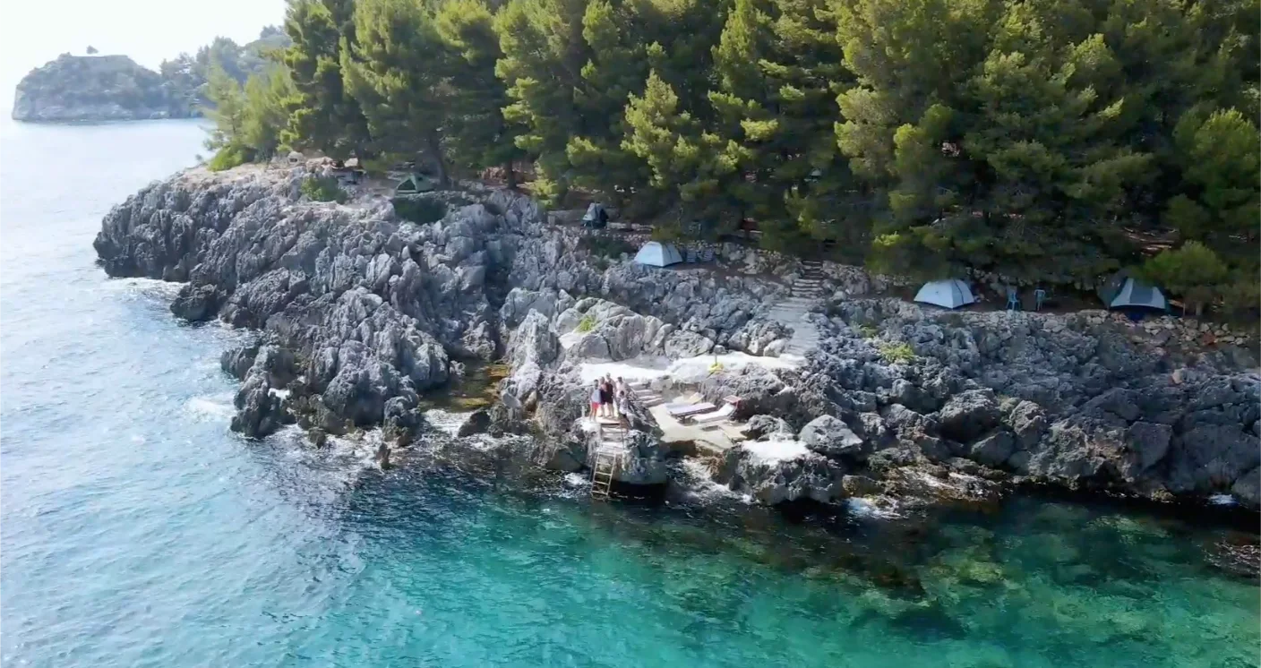 Tents pitched among pines on the rocky seaside headland at Pine Side Camp in Himara