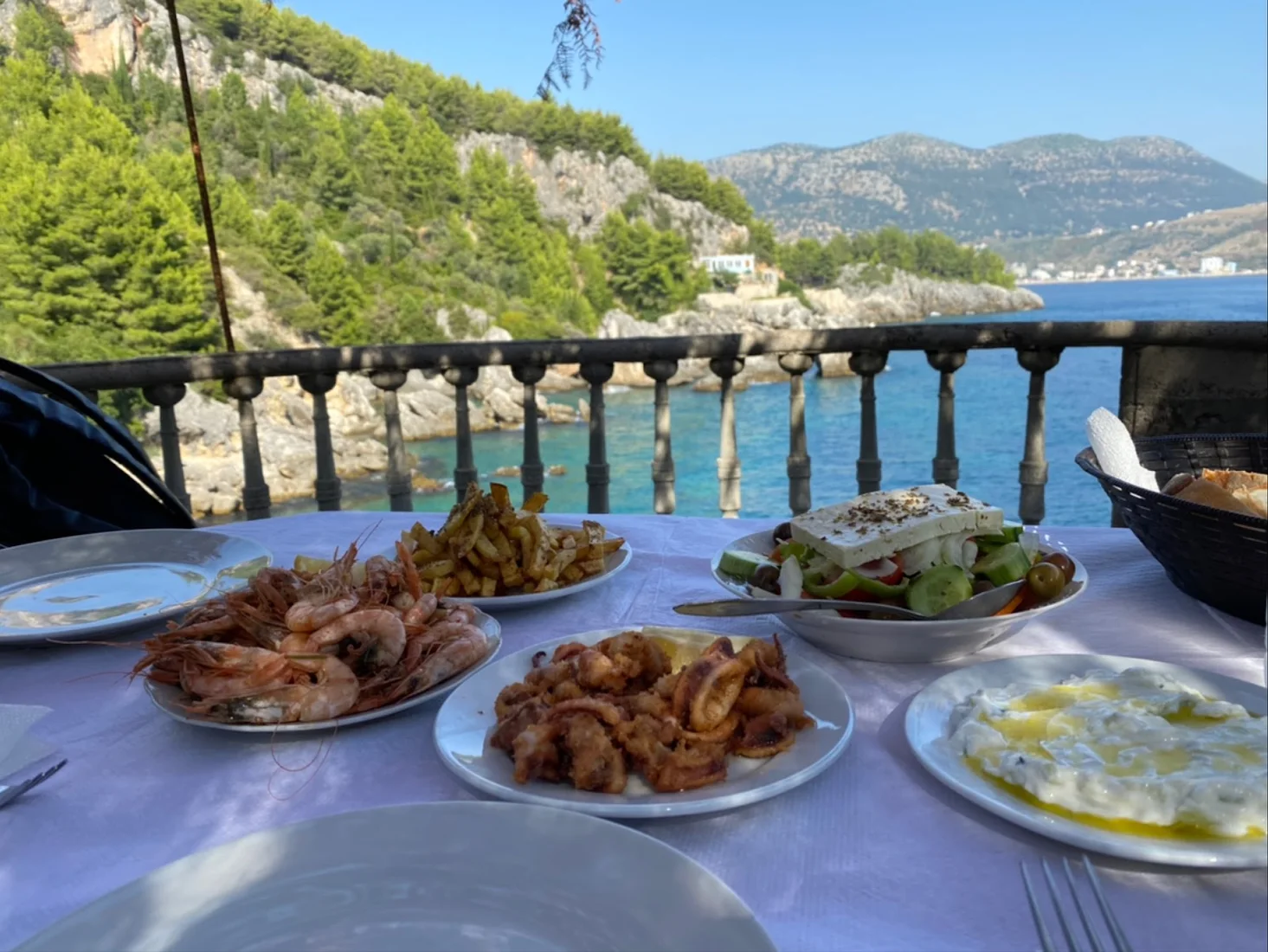 Table of fresh seafood and Greek salad with a view over a turquoise cove at Kilimani Retreat in Himara