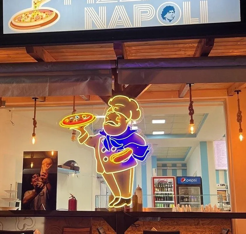 Covered terrace with the Pizza Napoli neon sign on a striped blue wall in Himara