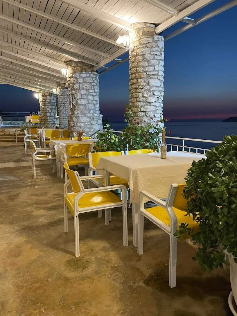 Sea-view terrace with yellow chairs at Tramonto Ristorante in Himara at dusk