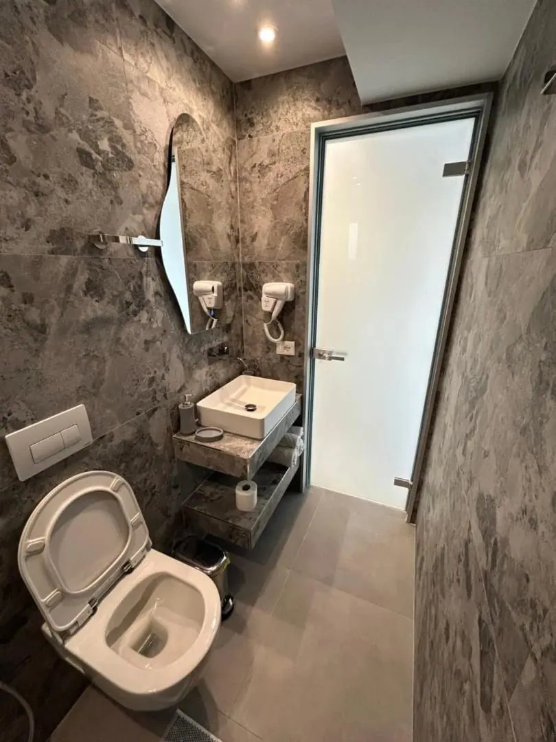 A bathroom in grey stone tile, a vessel basin on a stone shelf and a frosted glass door