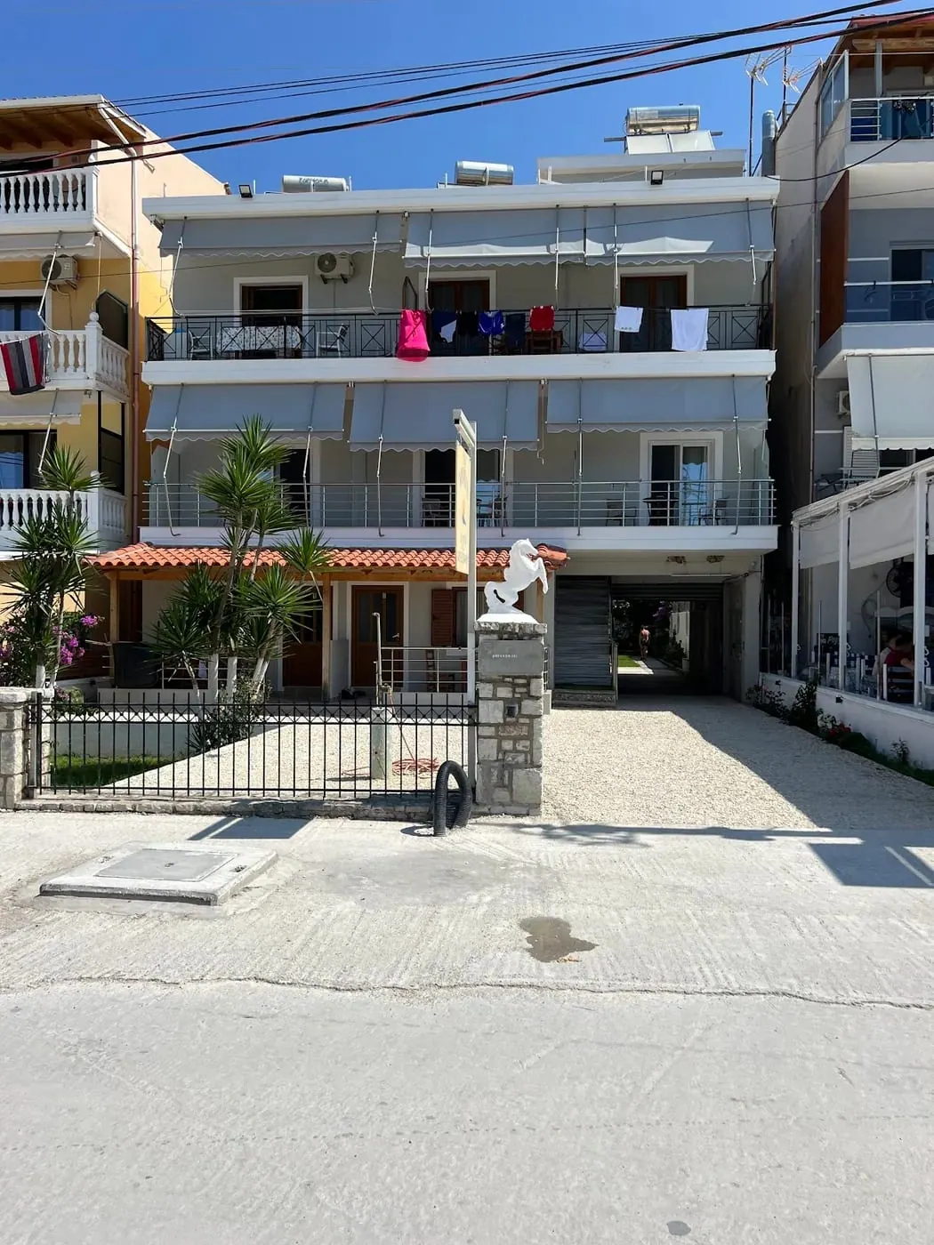 The front of Ionian View B&B from the beach road, awnings over every balcony and a gravel forecourt behind an iron railing