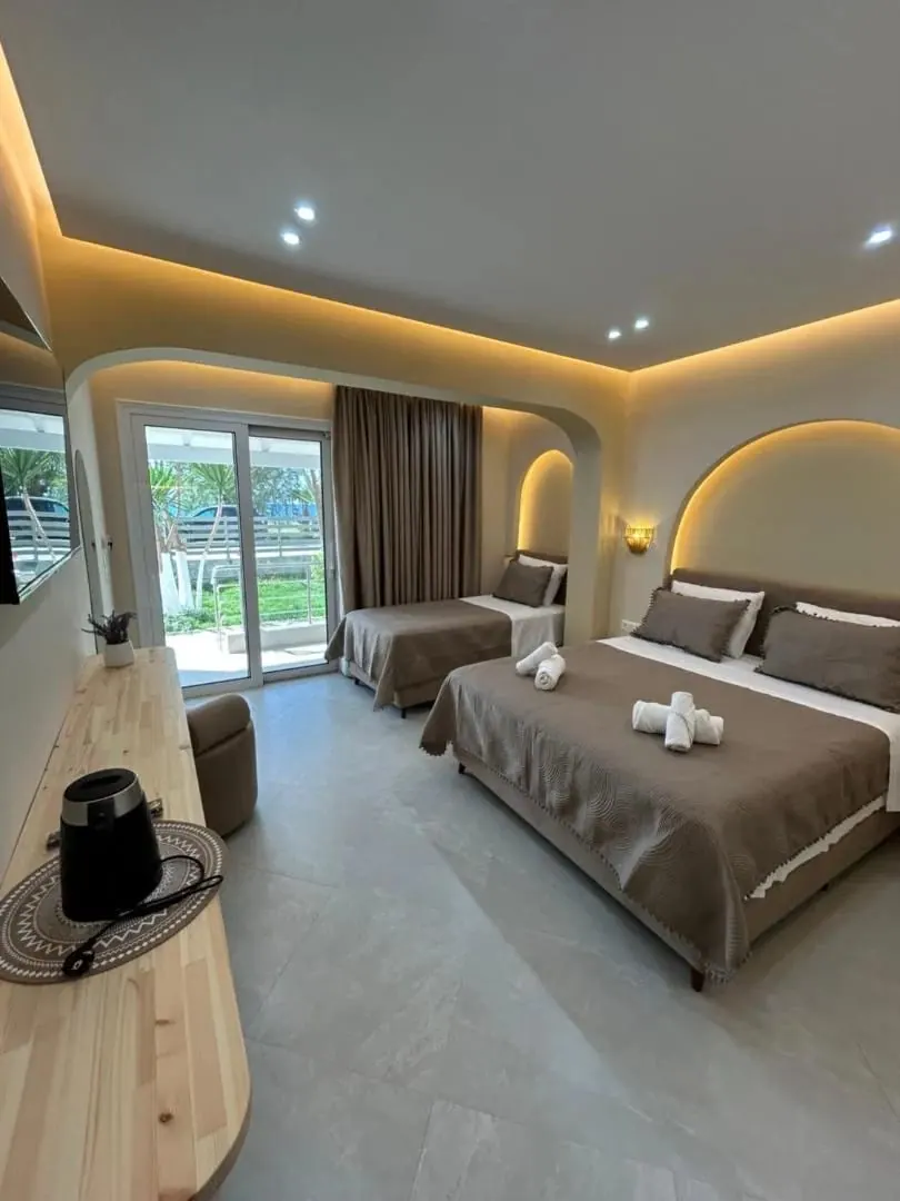 A triple room with two beds under arcs of light and sliding doors onto the lawn and the yuccas