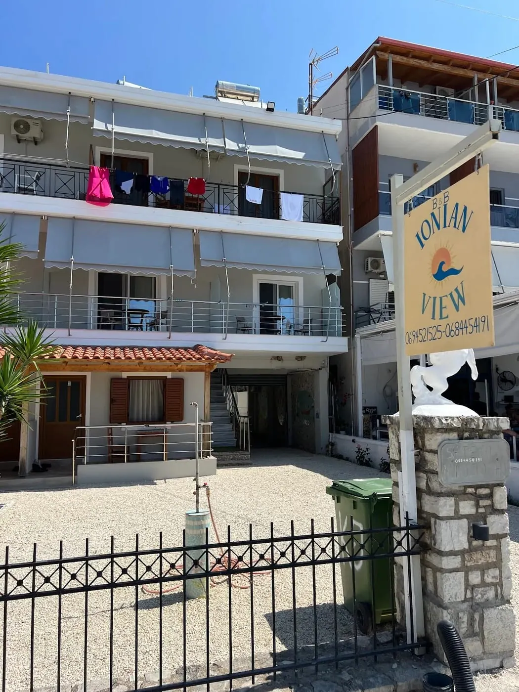 The hand-painted Ionian View B&B sign — a coral sun and a blue wave on a sand board — hanging on its bracket outside the building