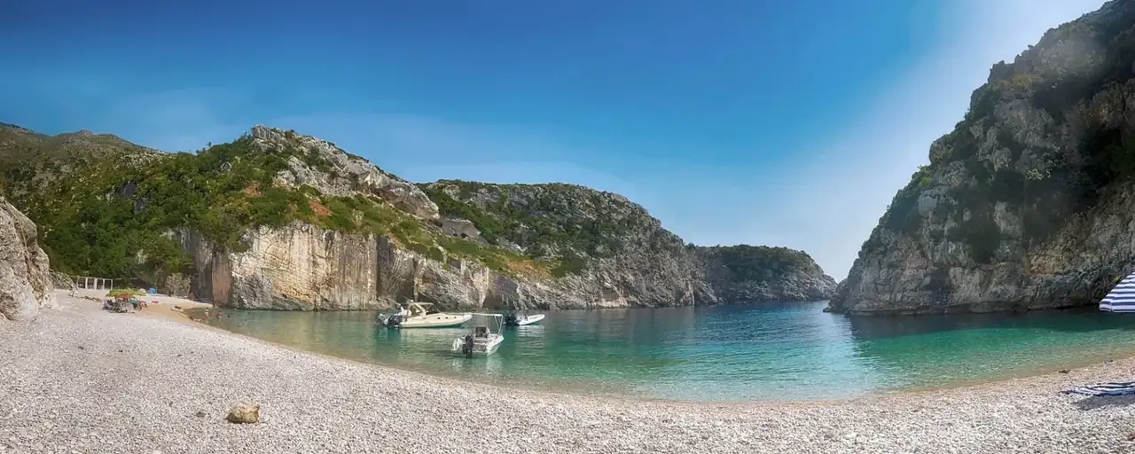 Boats moored on the pebbles at Gjipe beach beneath high grey cliffs