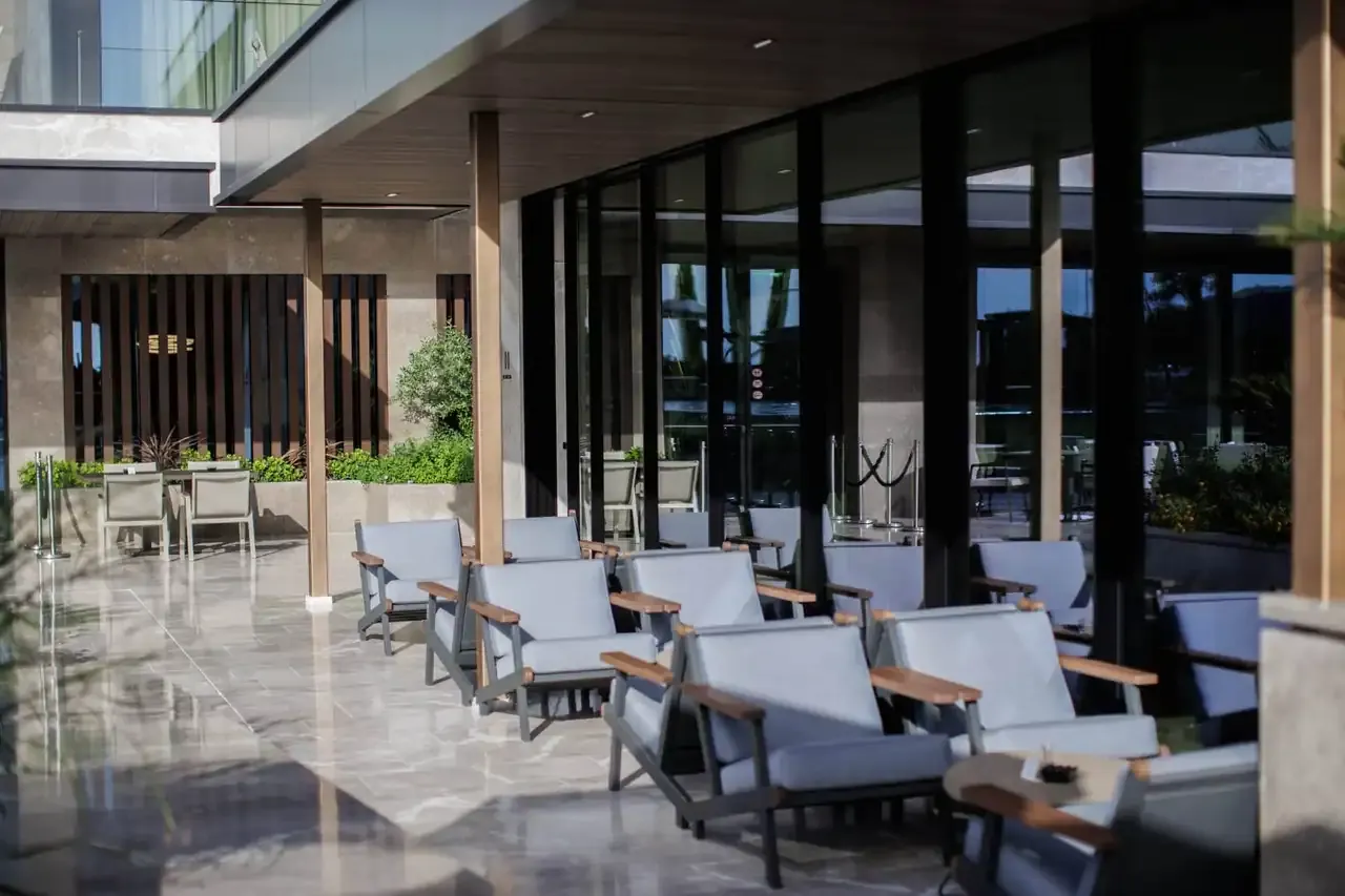 Sling lounge chairs with timber arms on the covered marble terrace at Prado, beside the glazing