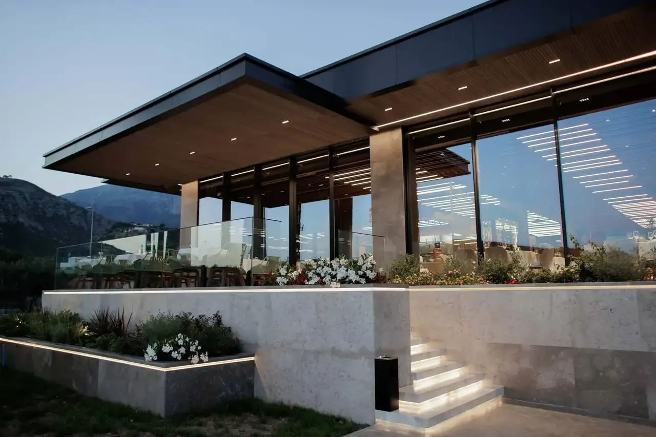 The glazed restaurant pavilion at Prado seen from outside in daylight, the mountains behind it