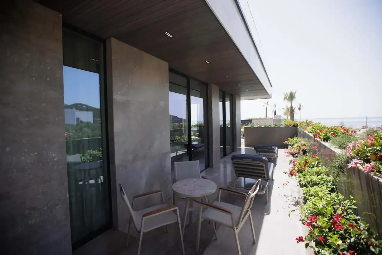 The long balcony of a sea-view Junior Suite, chairs and a table, loungers and flowering planters beyond