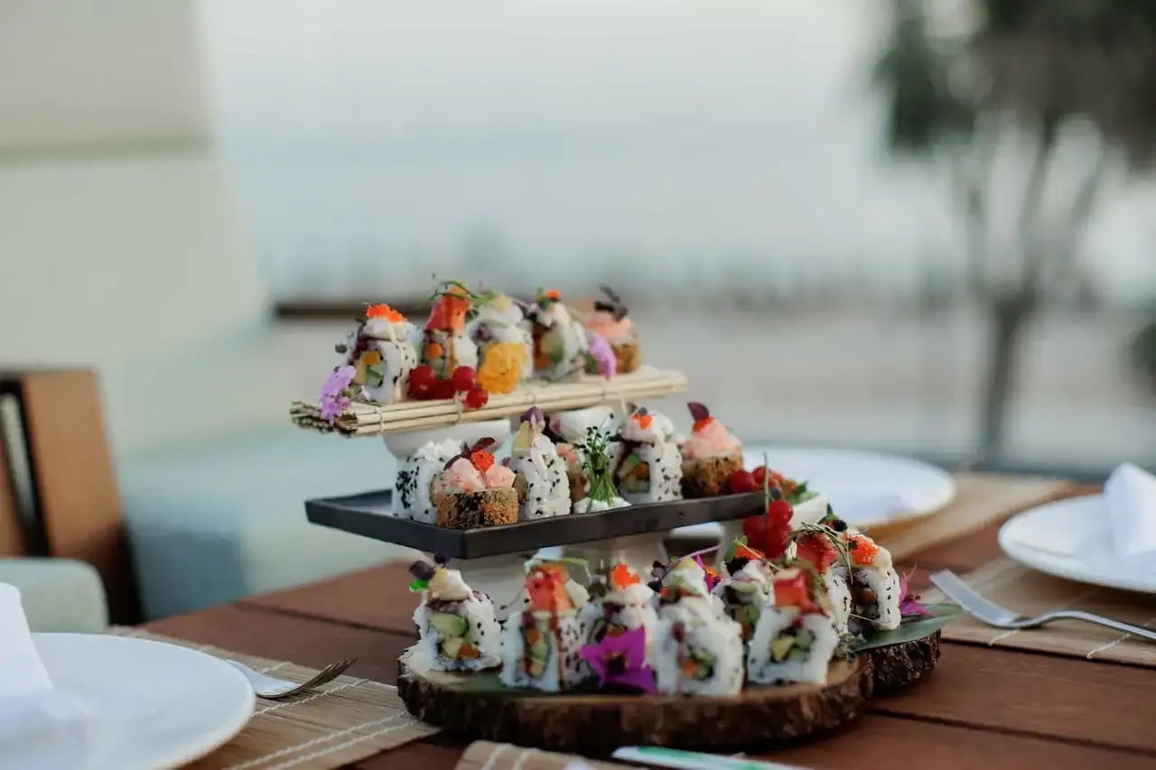 A three-tier stand of maki rolls at the sushi bar, the sea behind it