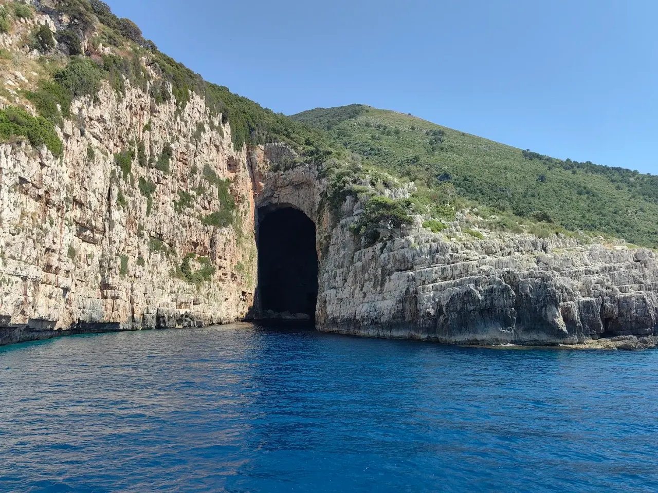 Arched sea cave entrance in a limestone headland on the Karaburun coast with deep blue water