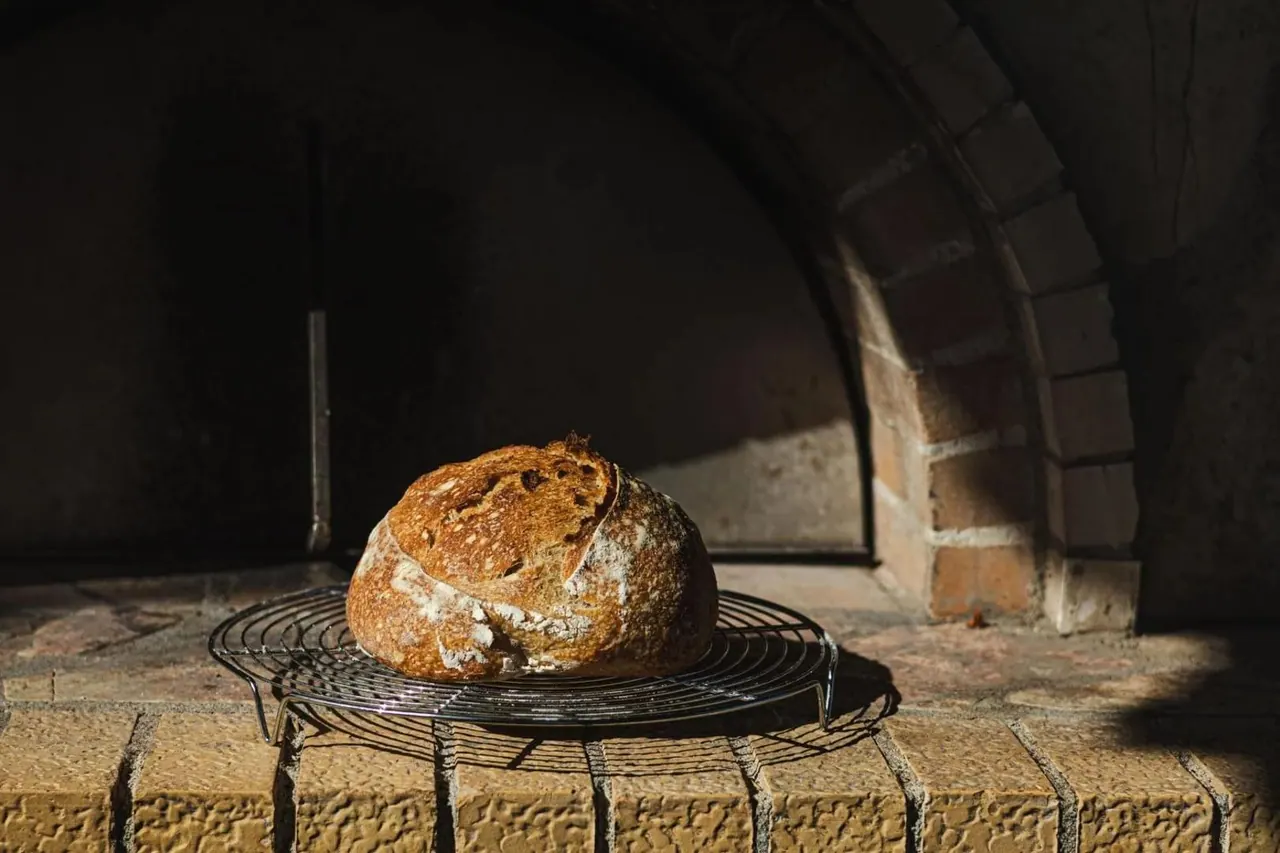 A round sourdough loaf cooling on a rack inside the mouth of the wood oven