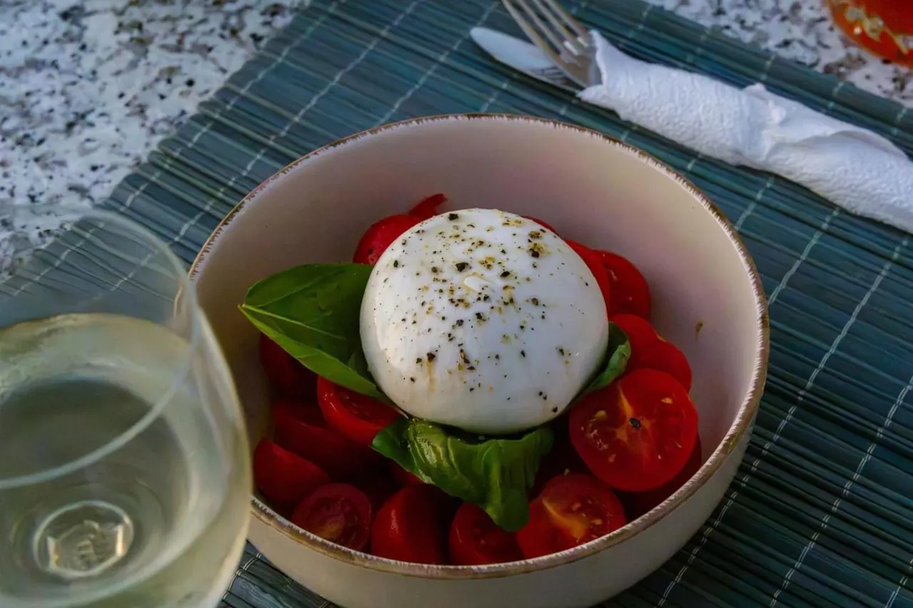 A bowl of burrata with cherry tomatoes and basil beside a glass of white wine