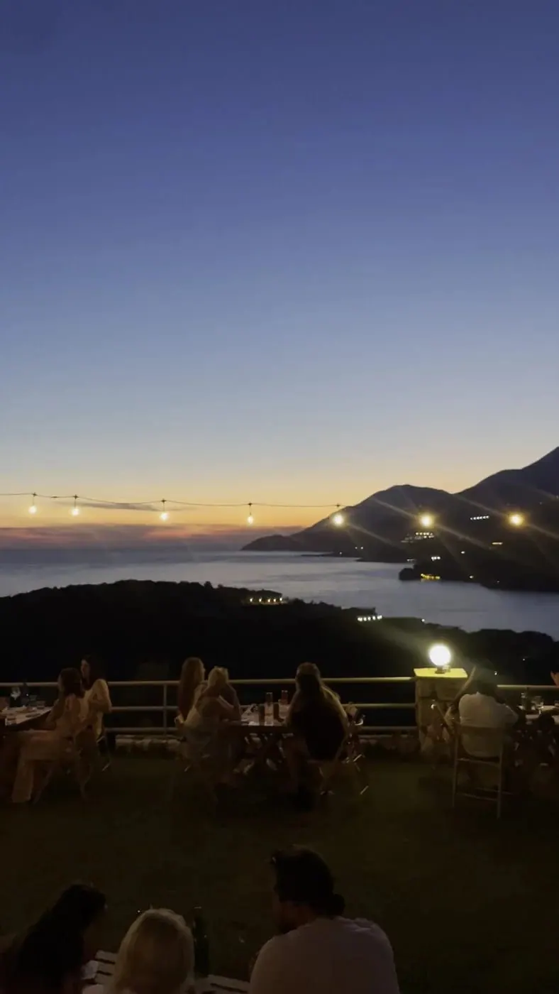 The bay at dusk from the terrace, lamps lit and the coastline fading to silhouette