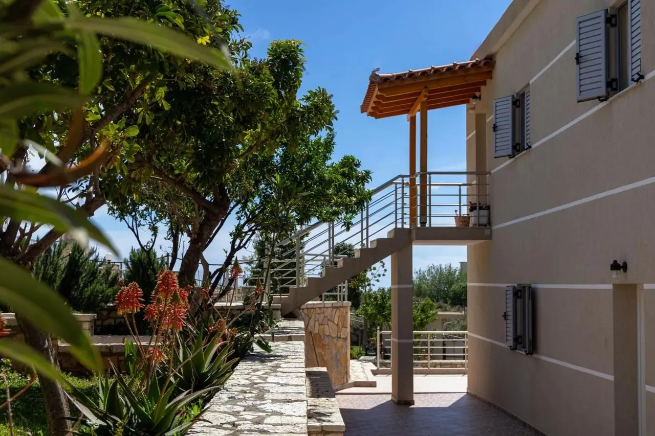 The guesthouse building in cream render behind flowering shrubs and a stone path