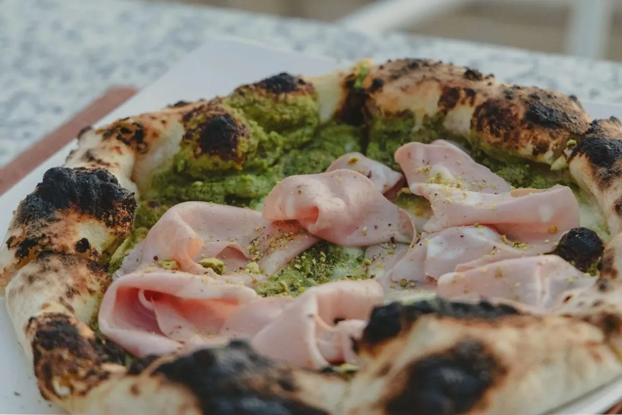 A pesto-based pizza topped with folded slices of mortadella and crushed pistachio